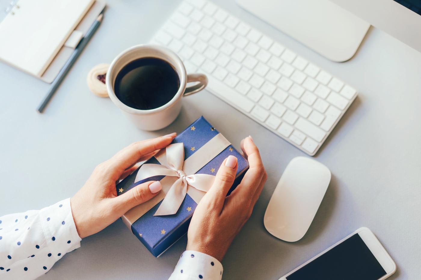 Hands placing a wrapped gift box with a ribbon on an office desk